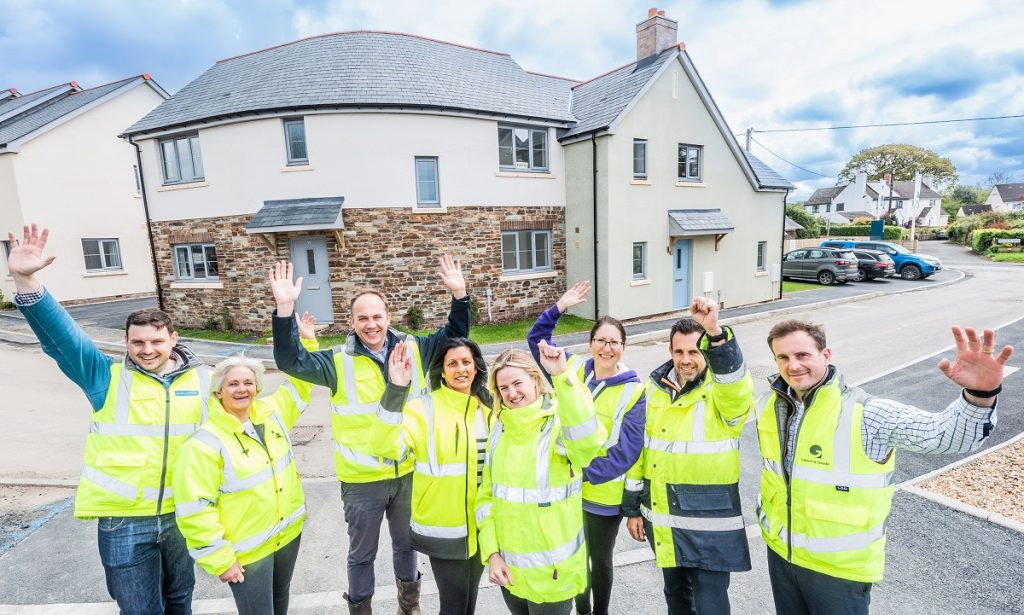 group of people standing in front of some new houses, cheering with arms in the air